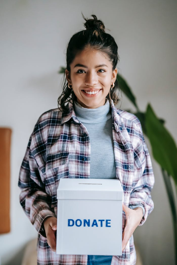services-01 Cheerful woman holding a box labeled Donate indoors, symbolizing charity and kindness.