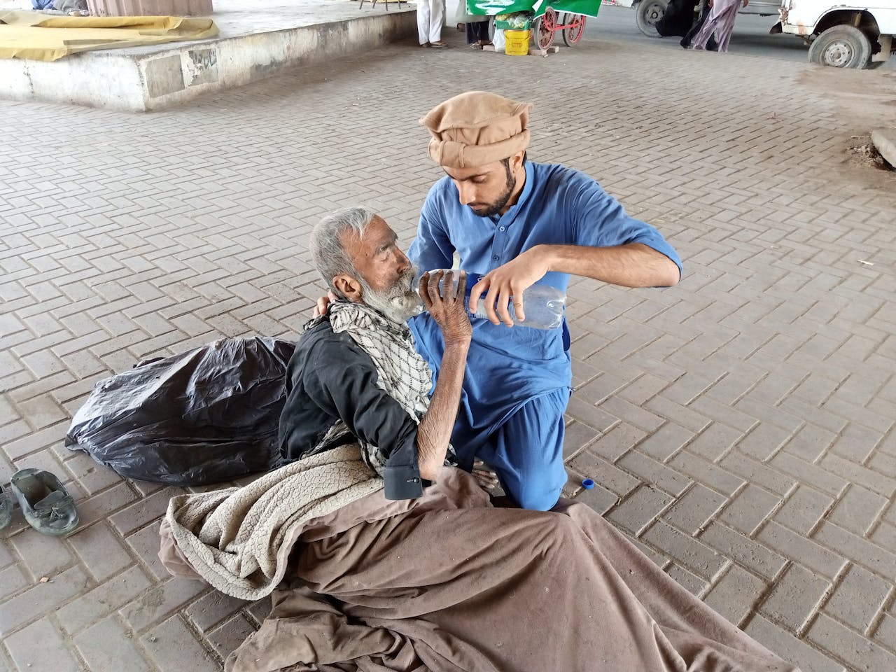 impact-img A young man helps a homeless senior by giving water outdoors in Karachi, Pakistan.