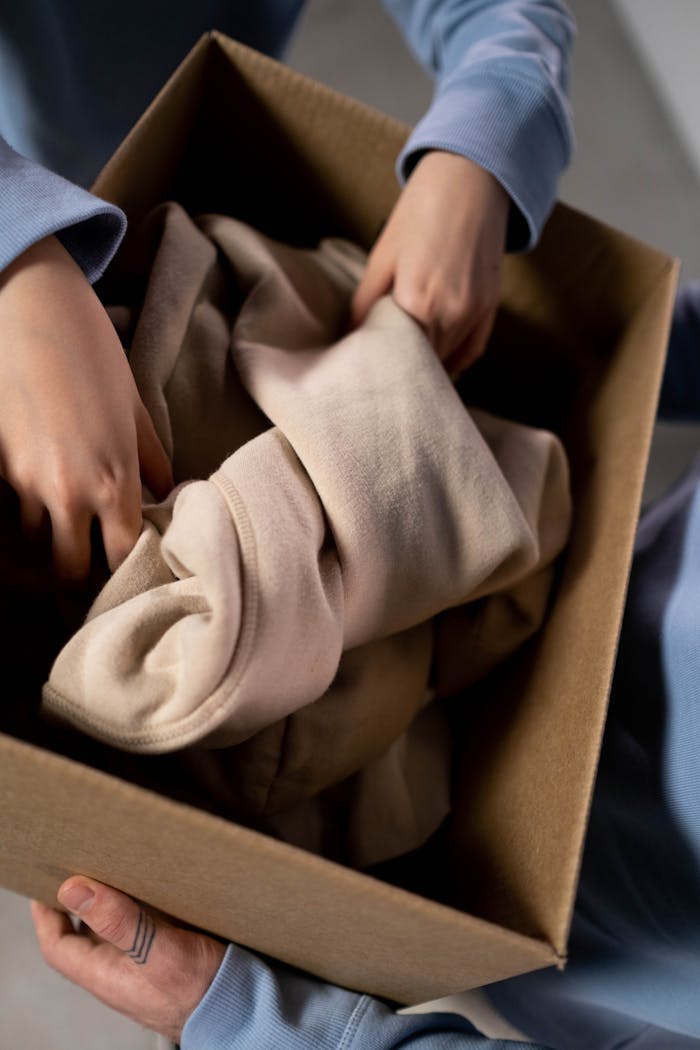 services-04 Close-up of hands sorting clothes into a cardboard box for charity donations.